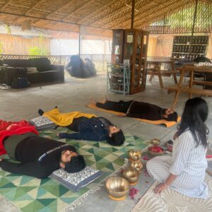 A sound therapist guiding a group during a sound therapy session with participants lying on mats surrounded by Tibetan singing bowls.